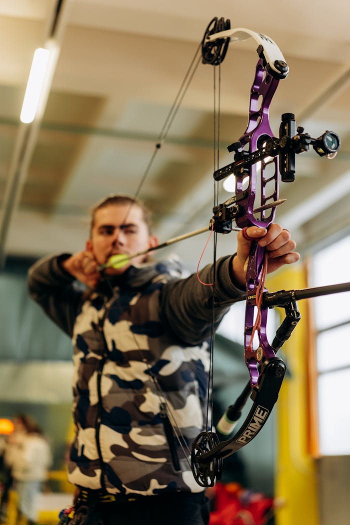 portfolio-05 A man intensely focuses on aiming a purple compound bow at an indoor archery range.