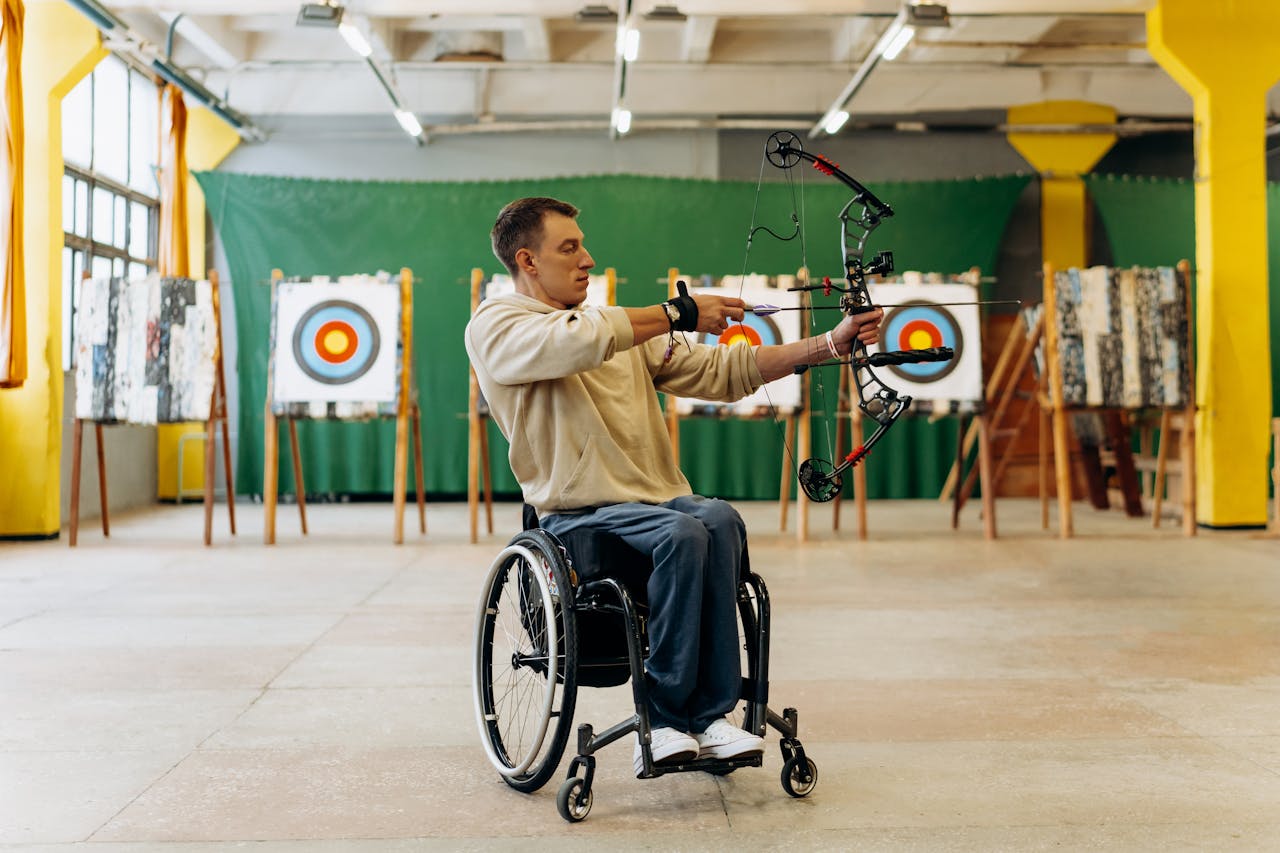 portfolio-04 Focused young man in a wheelchair practicing archery indoors, aiming with determination at a target.